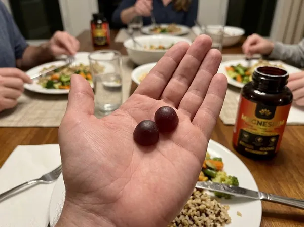 Two MAGNESIUM gummies in an open hand at the dinner table, next to the bottle