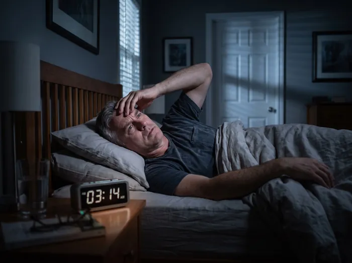 Man lying awake in bed at 3:14 a.m., rubbing his forehead